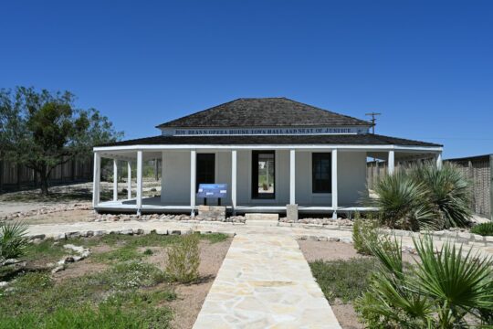 A white house with a wrap-around porch under blue sky.